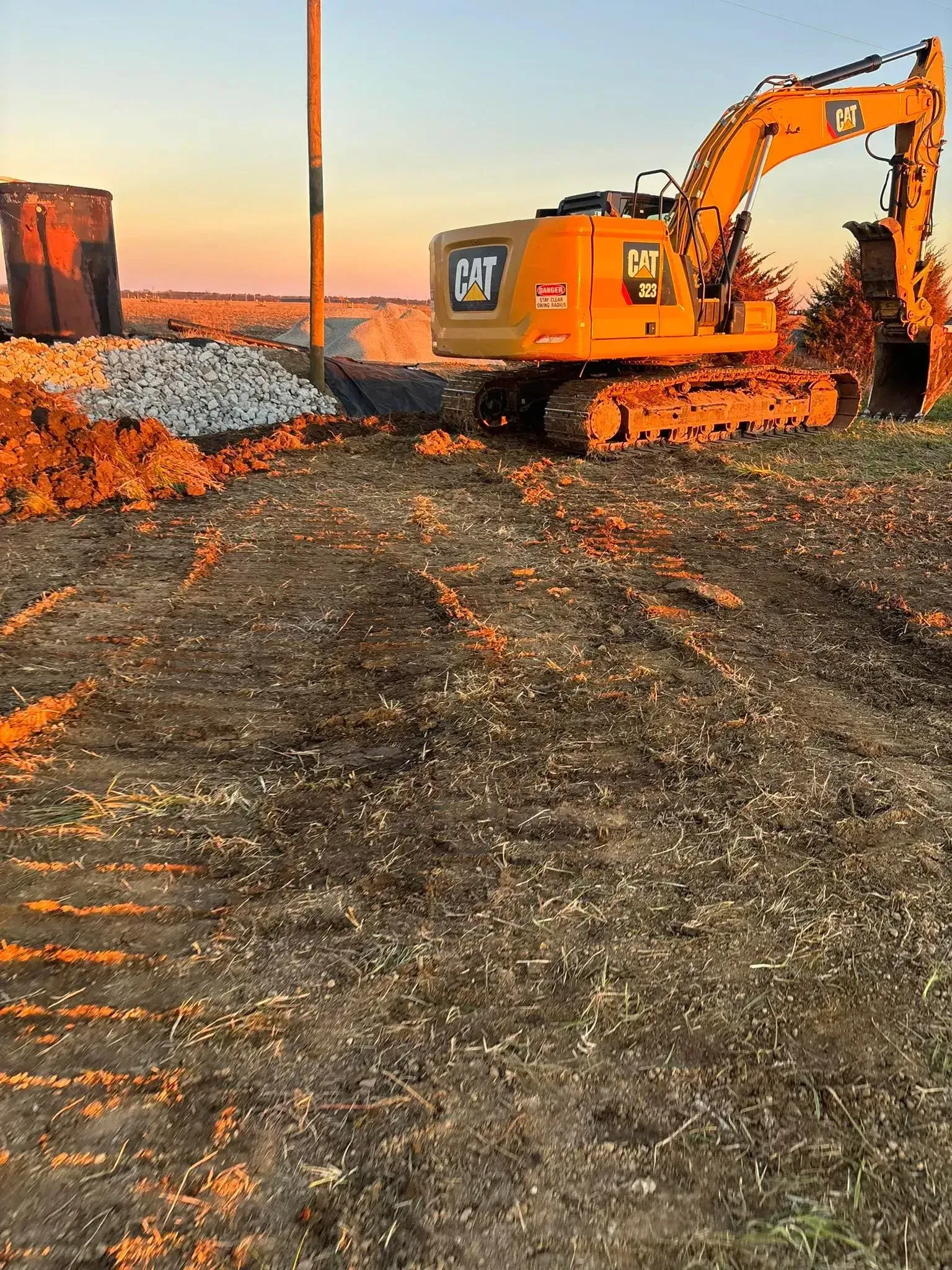 Yellow CAT excavator on a construction site, with dirt, debris, and sunset sky.