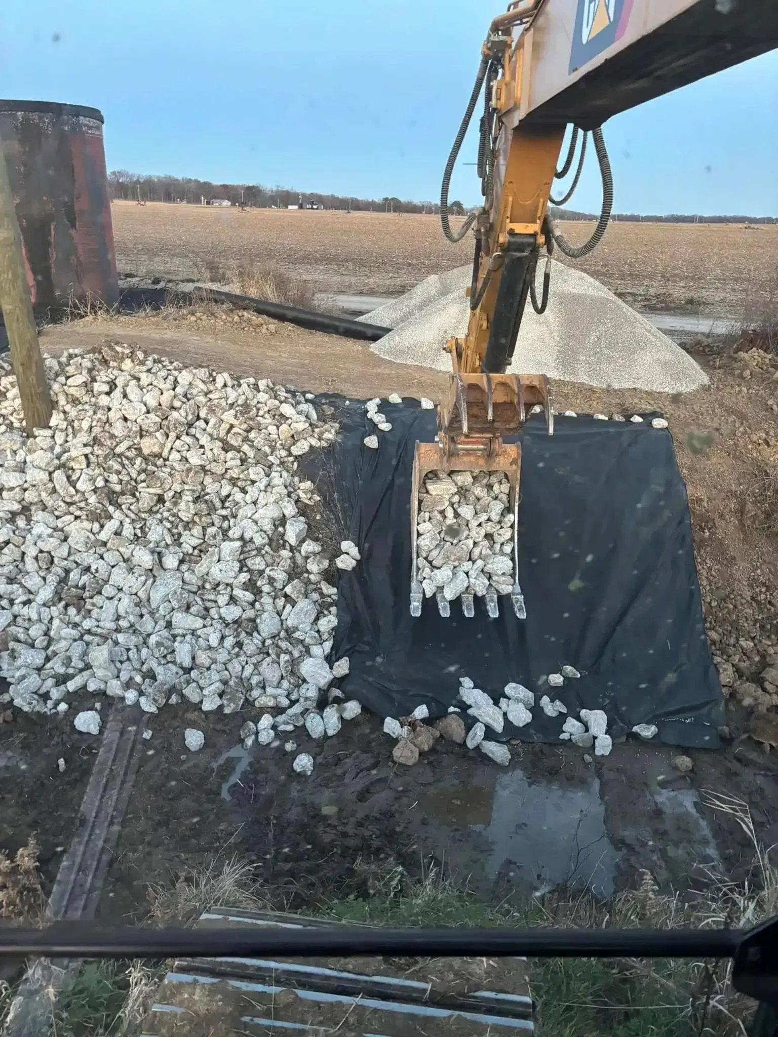 An excavator placing white rocks on black fabric, in a field.