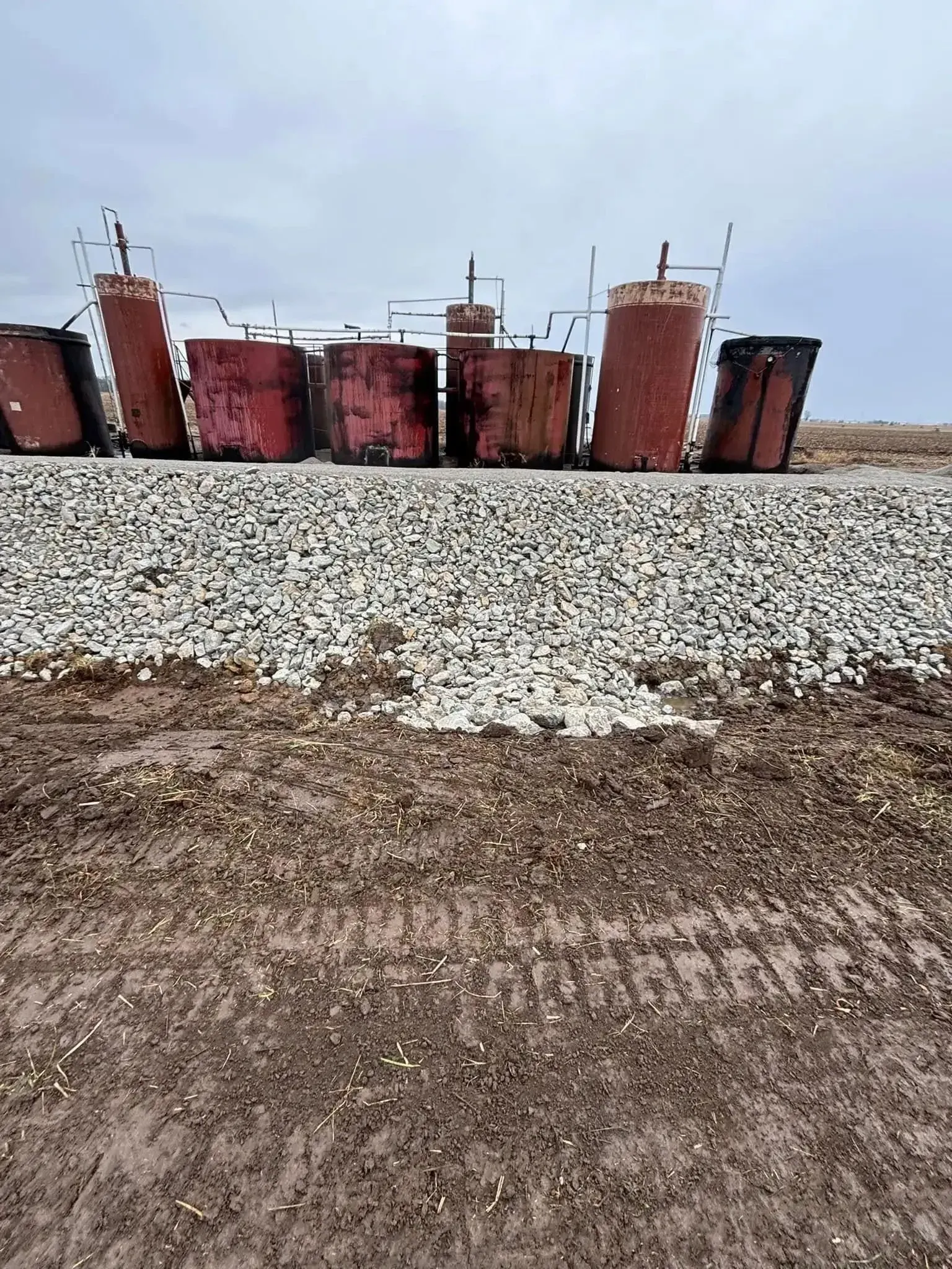 Red industrial containers on a pile of gravel, on a muddy, overcast day.