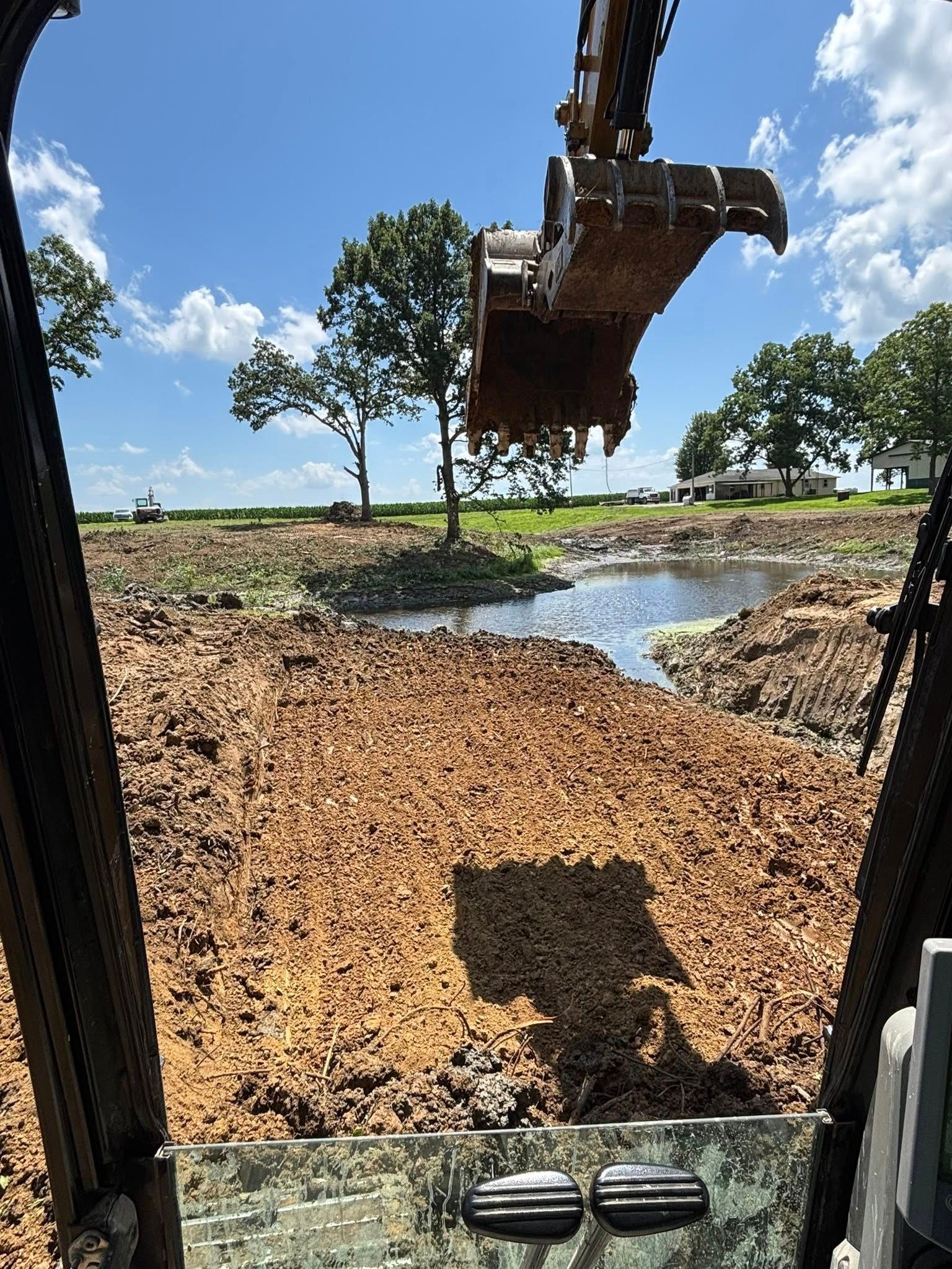 Excavator digging in muddy terrain, with a water body visible in the background under a blue sky.