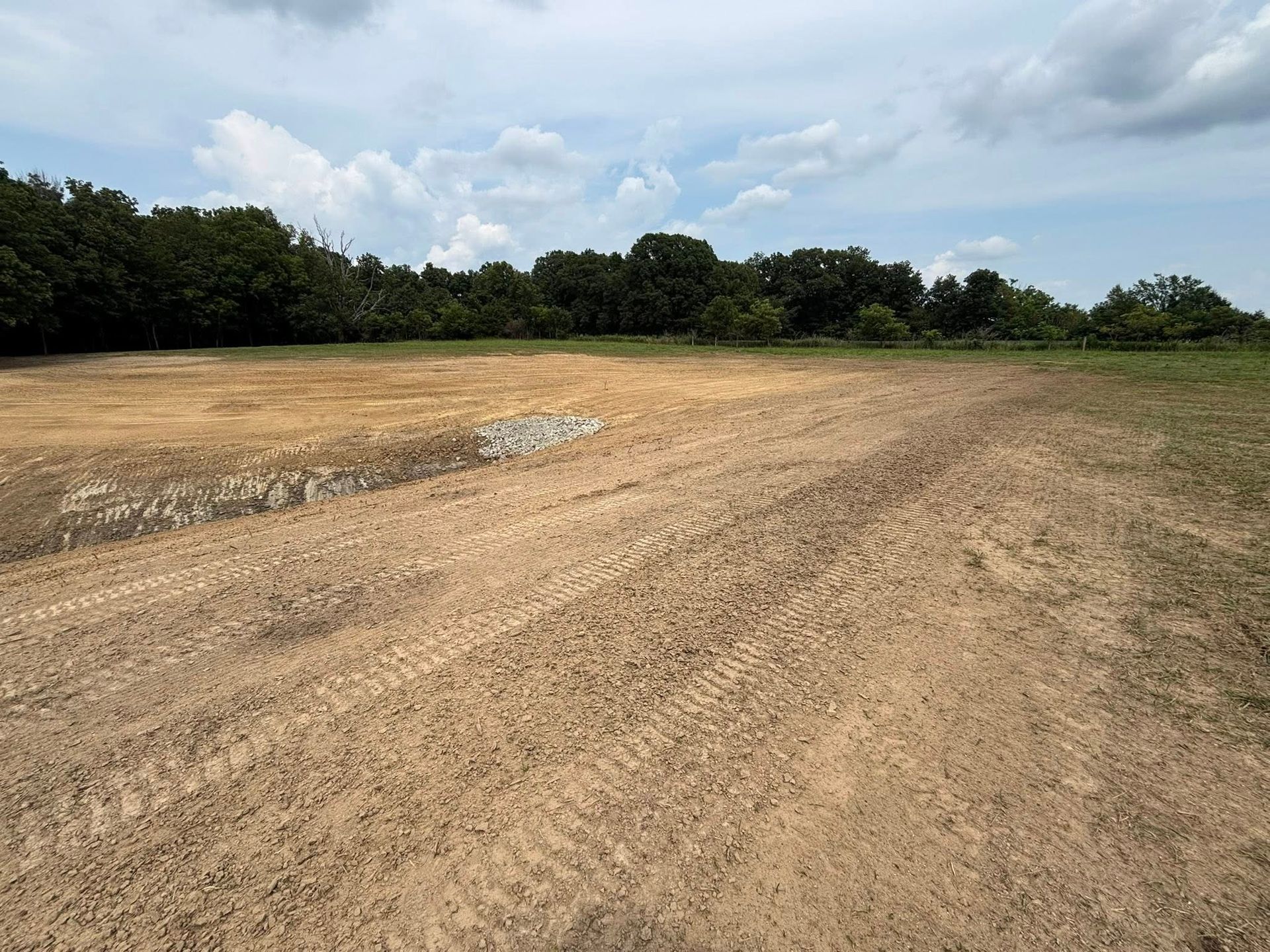 Dirt field, possibly cleared for construction, under a cloudy sky, with trees in the background.