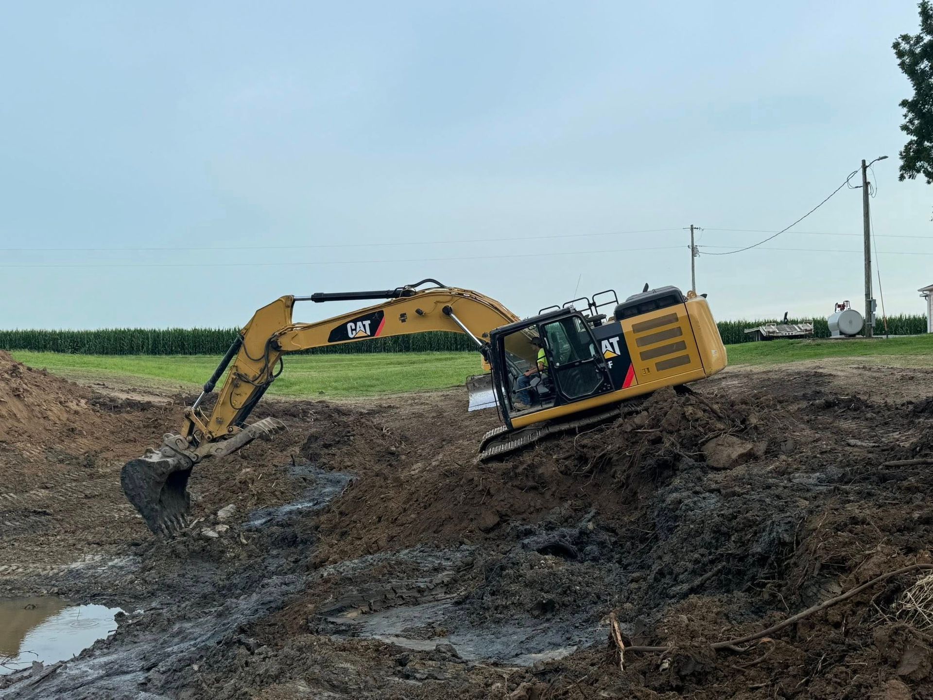 Yellow excavator digging in muddy earth near a field.