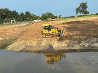 Yellow bulldozer grading a hillside into a body of water.