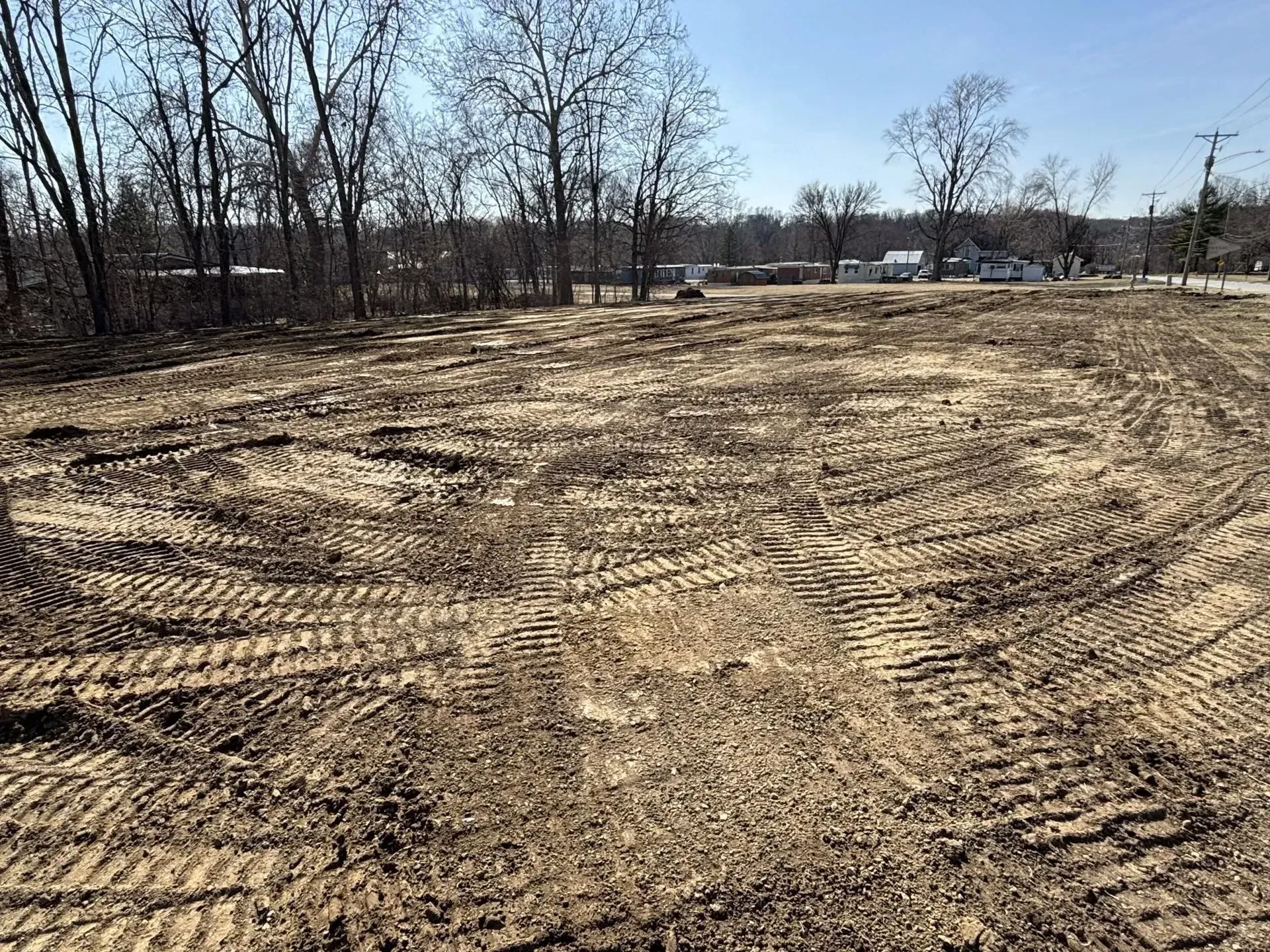 Cleared construction site with tire tracks in dirt, trees in the background.