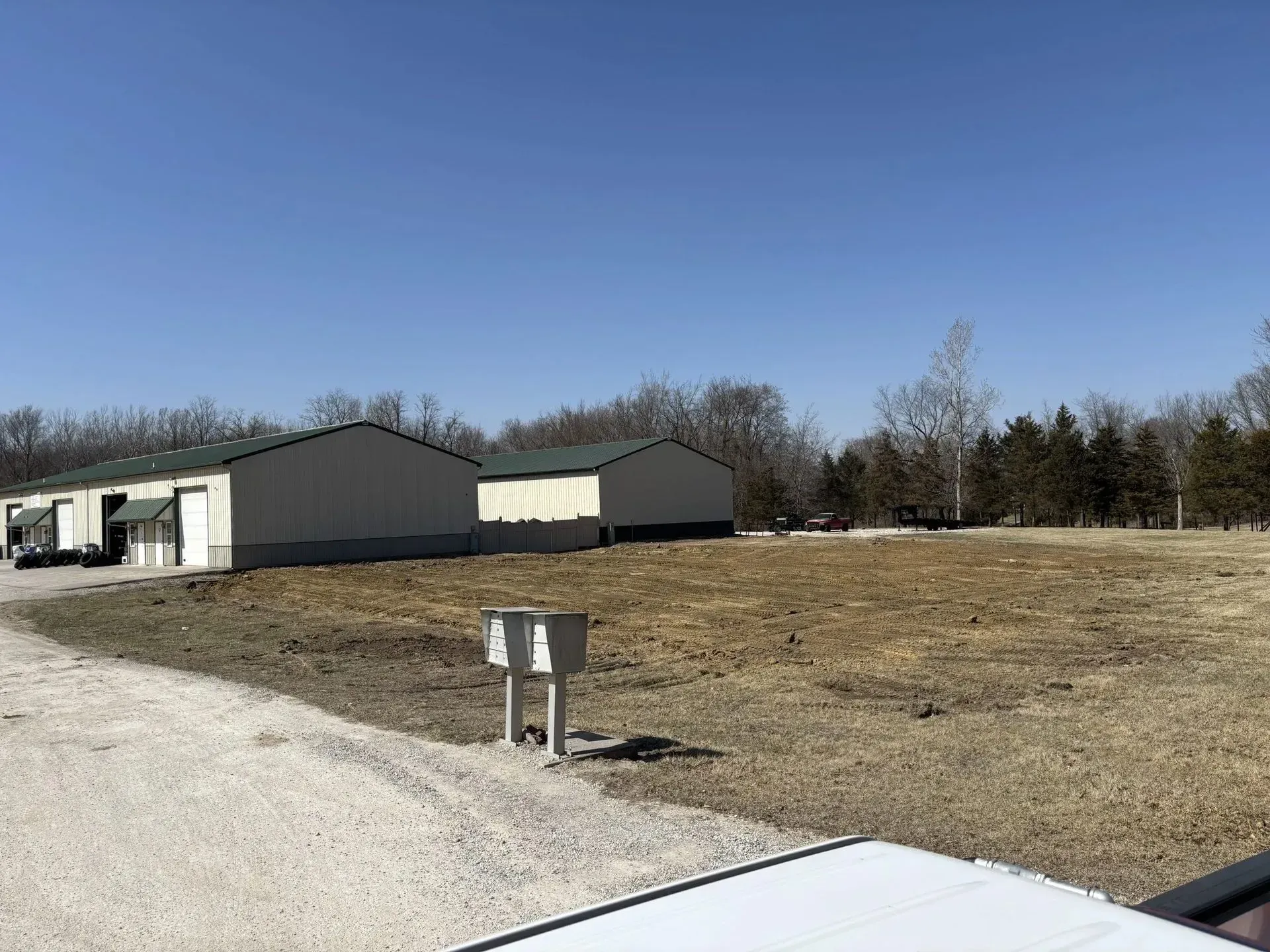 Buildings with light-colored siding and green roofs on a brown field under a blue sky.