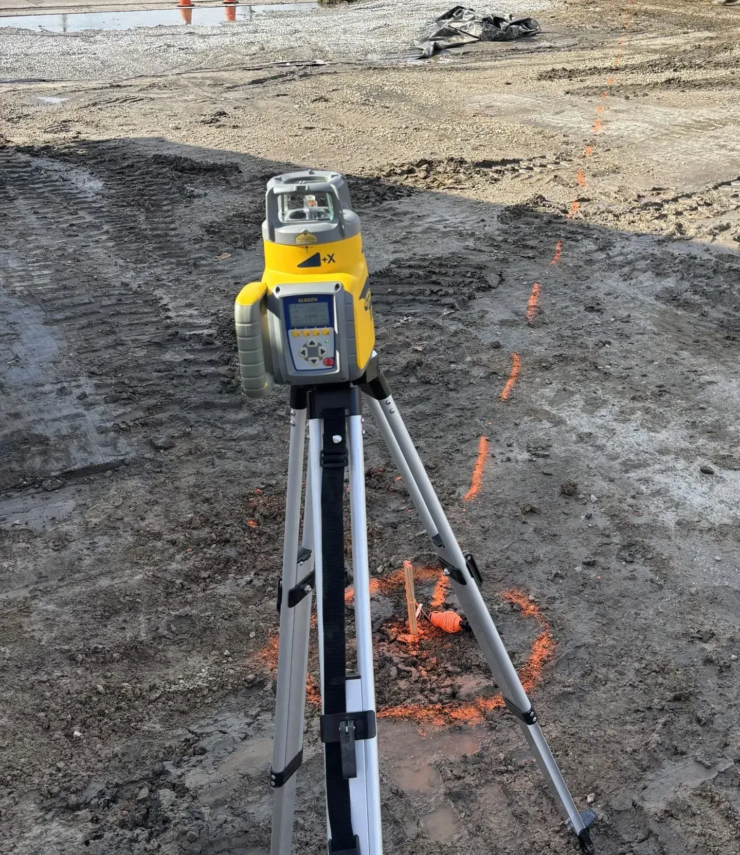 Yellow laser level on tripod in dirt, used for construction leveling, with orange markings.