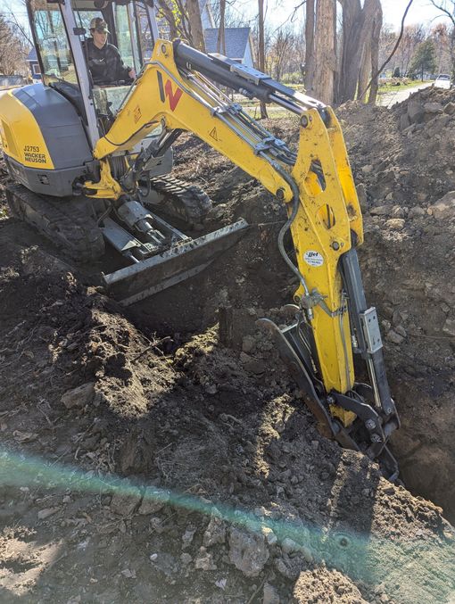 Yellow excavator digging a trench in brown soil, operator visible in the cab.