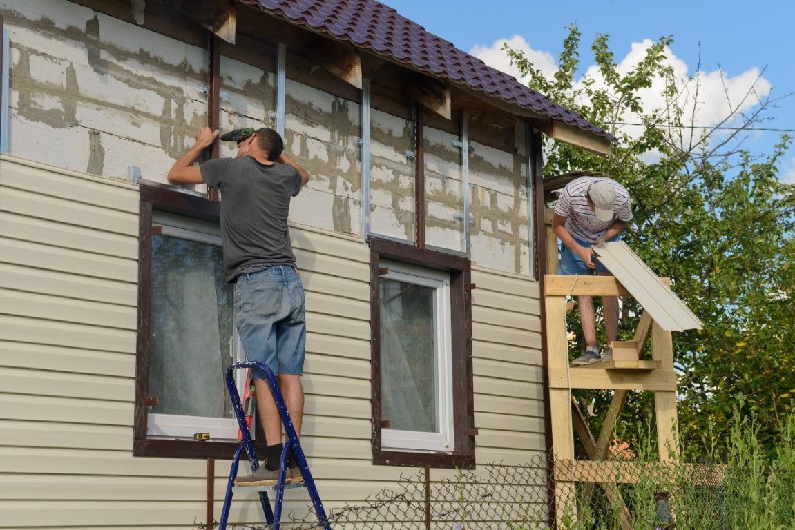 Two men on ladders working on the exterior of a home