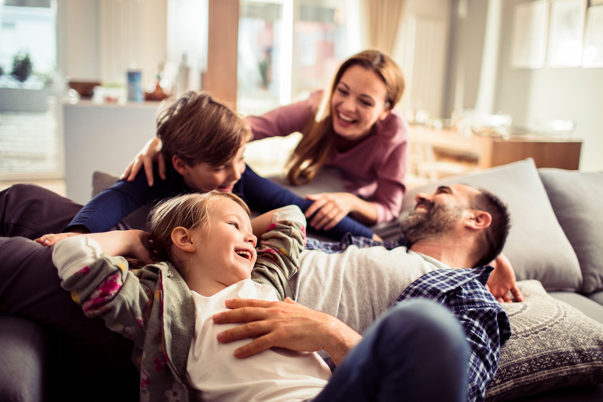 Family of four laughing together on a couch in a living room. Family of four laughing together on a couch in a living room.