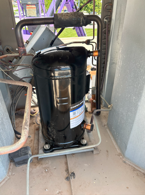 Black HVAC compressor on a metal base, copper pipes attached, inside a grey unit.