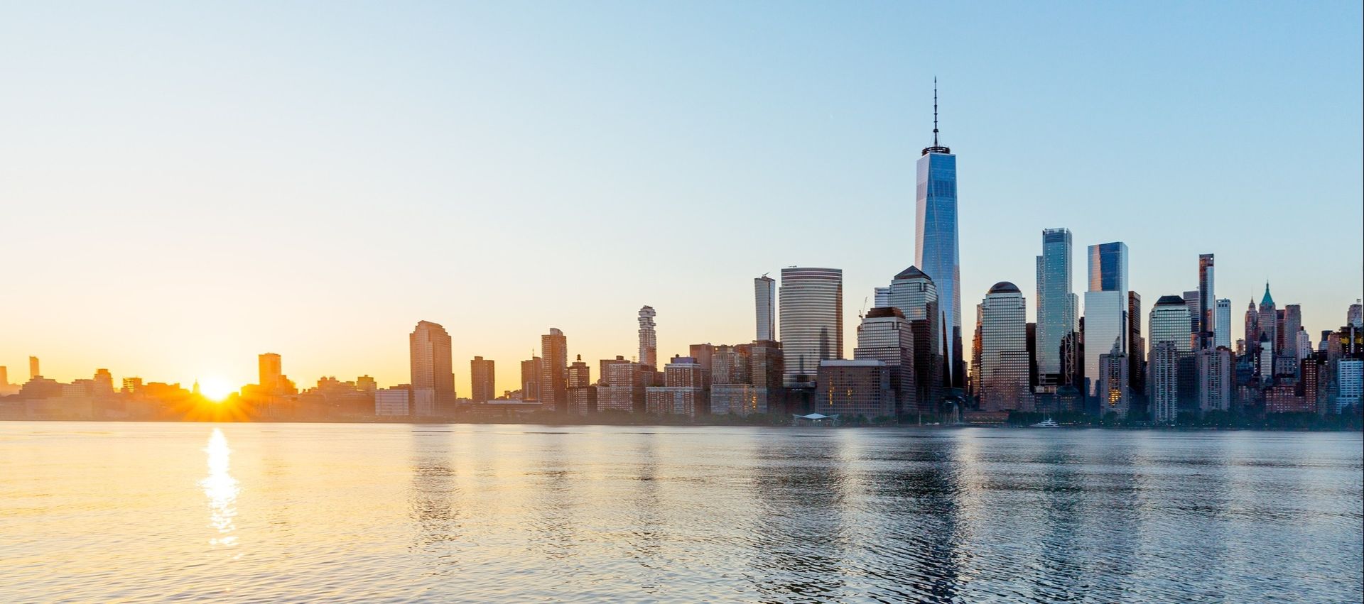 The skyline of new york city is reflected in the water at sunset.