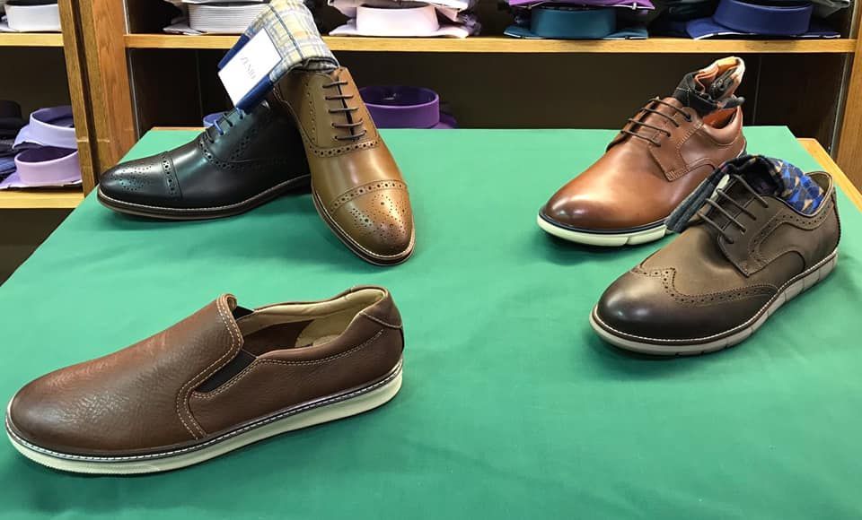 Four pairs of men's shoes on a green surface: brown slip-ons, brogues, and leather dress shoes.