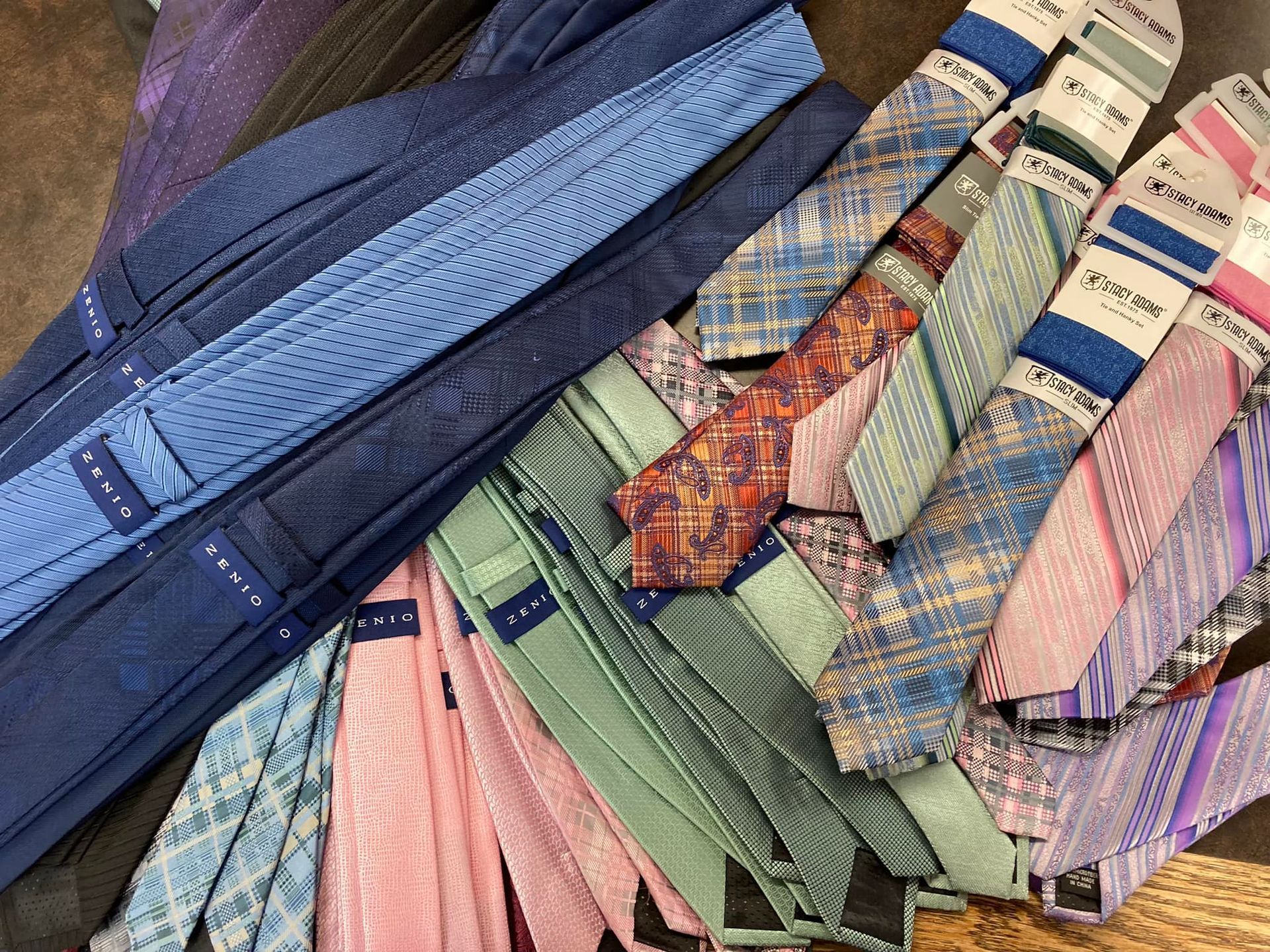 Collection of colorful neckties, stacked and displayed. Various patterns and shades including blue, pink, and patterned designs.