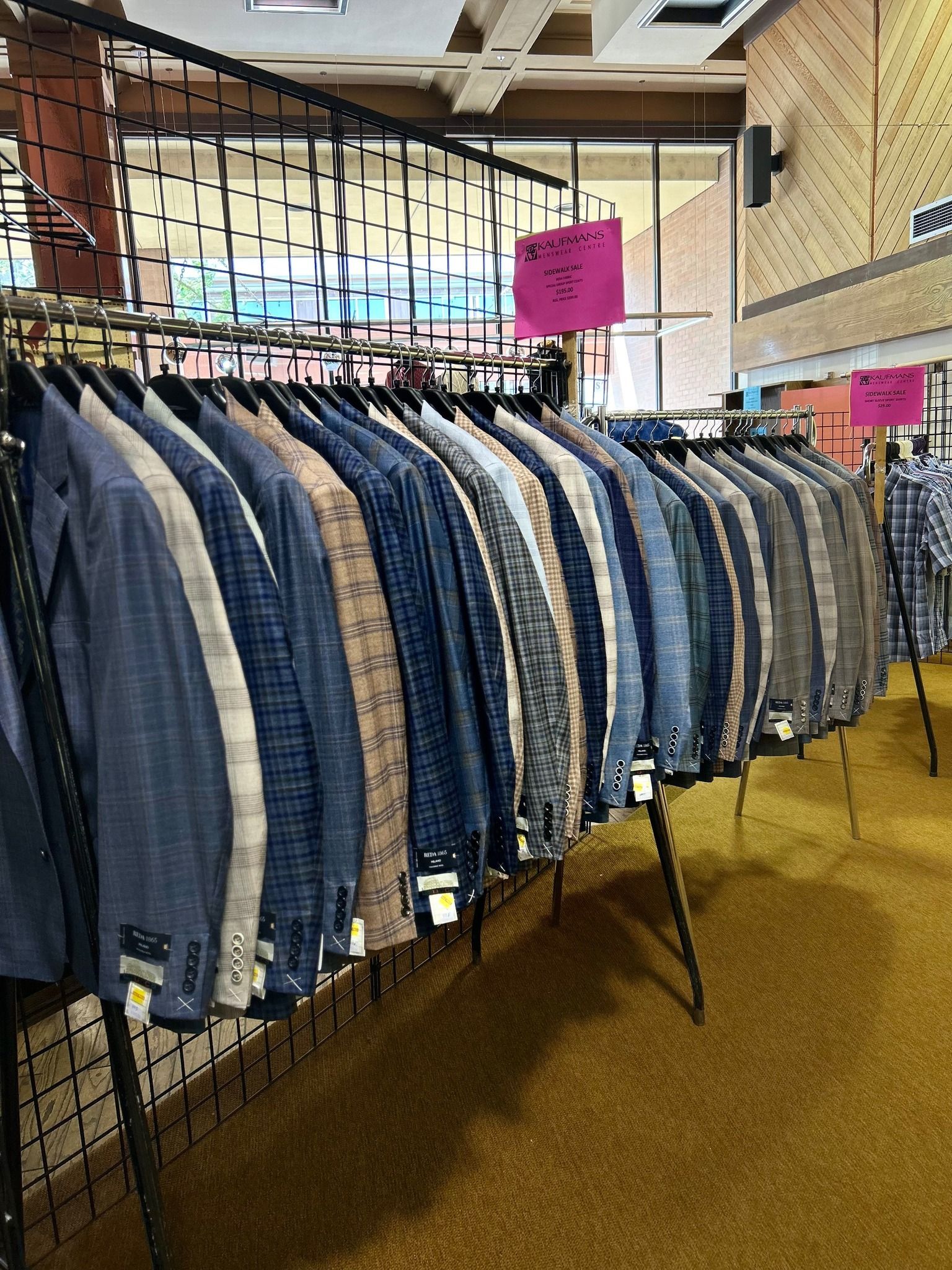 Row of jackets hanging on a rack inside a store; jackets are various colors, a sign is visible.