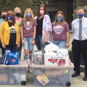 Group of people standing behind large plastic totes that are filled with donated supplies