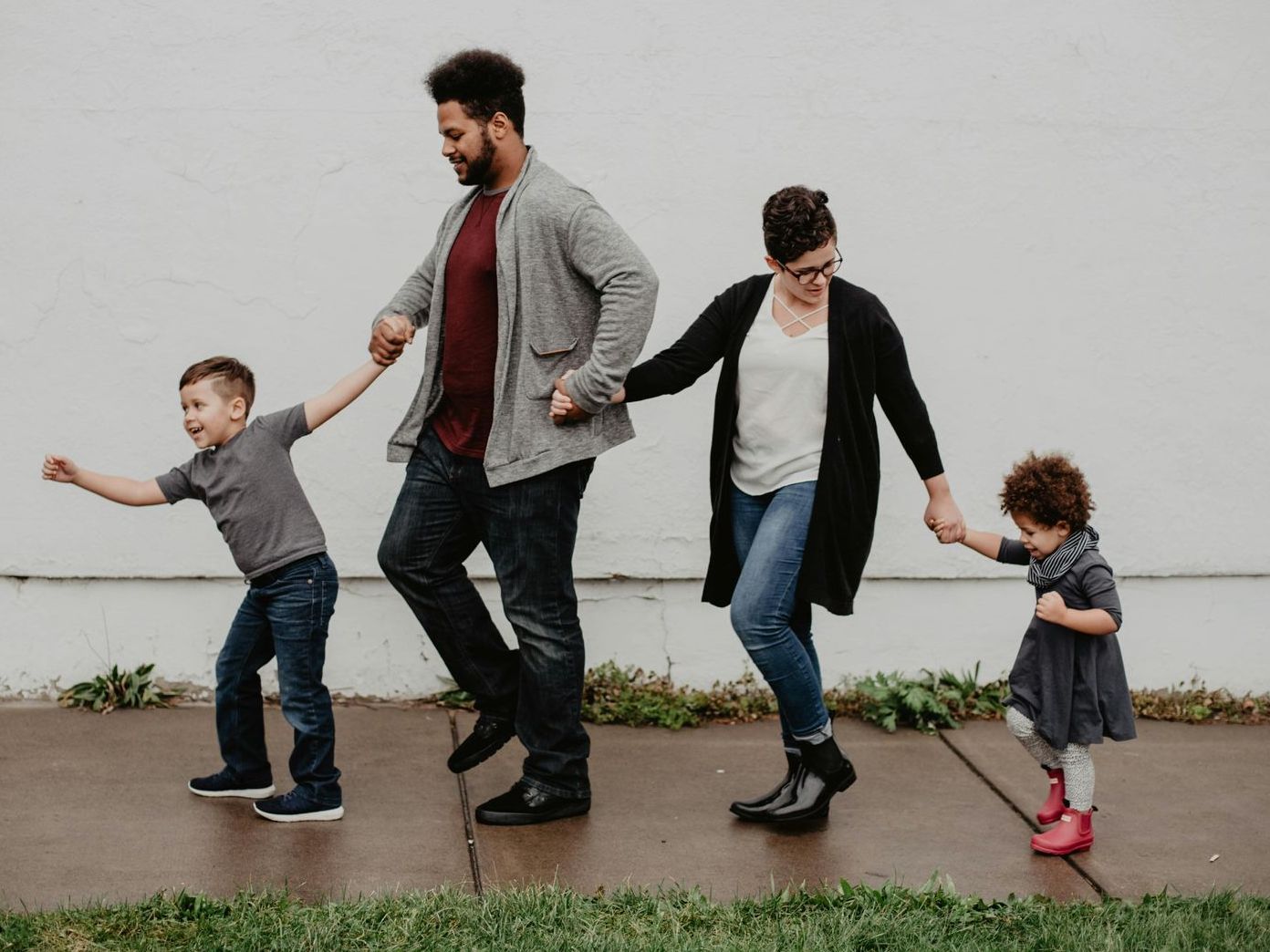 A family is walking down a sidewalk holding hands.