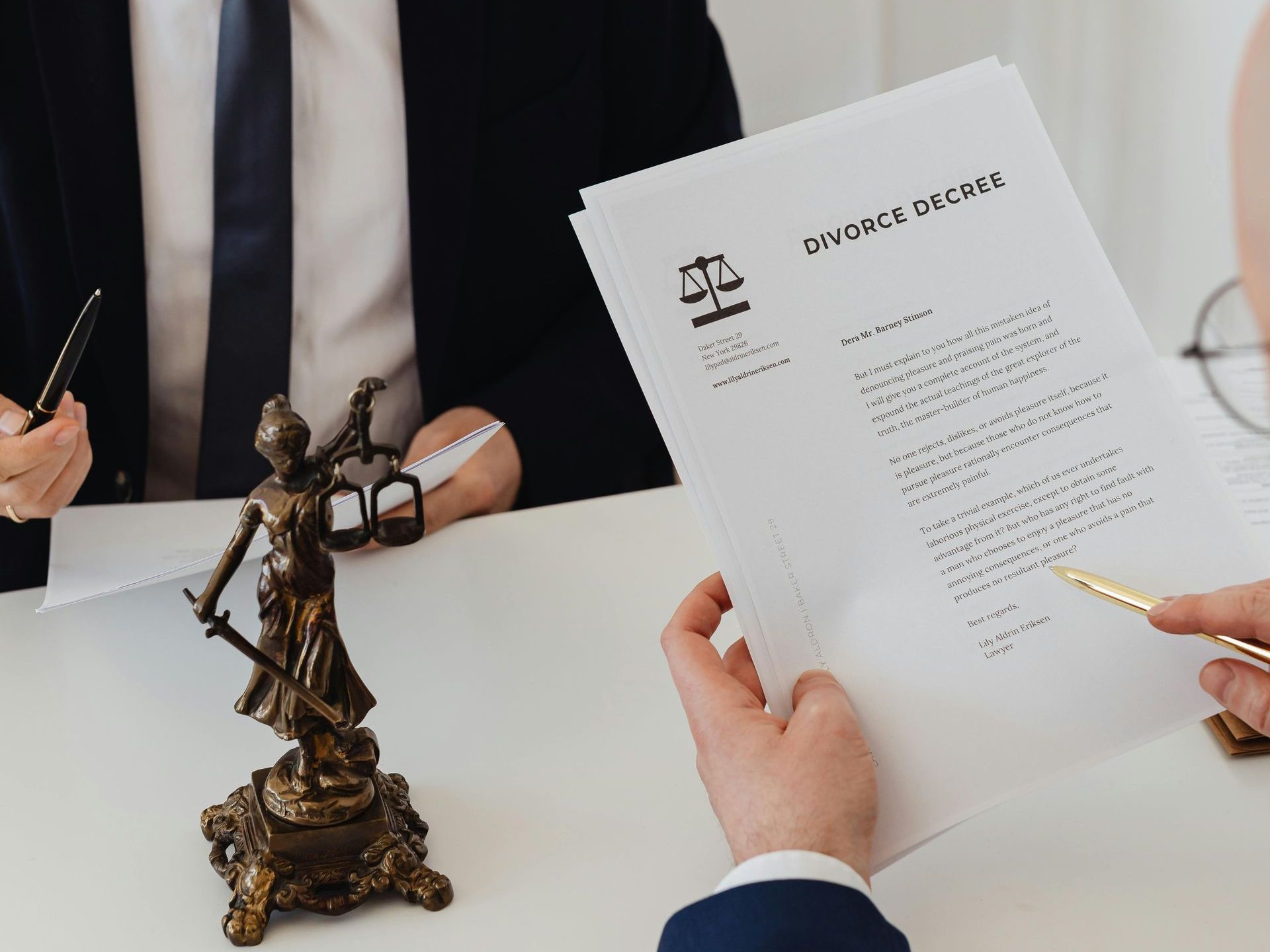 A statue of lady justice is sitting on a table next to a person holding a pen and a piece of paper.