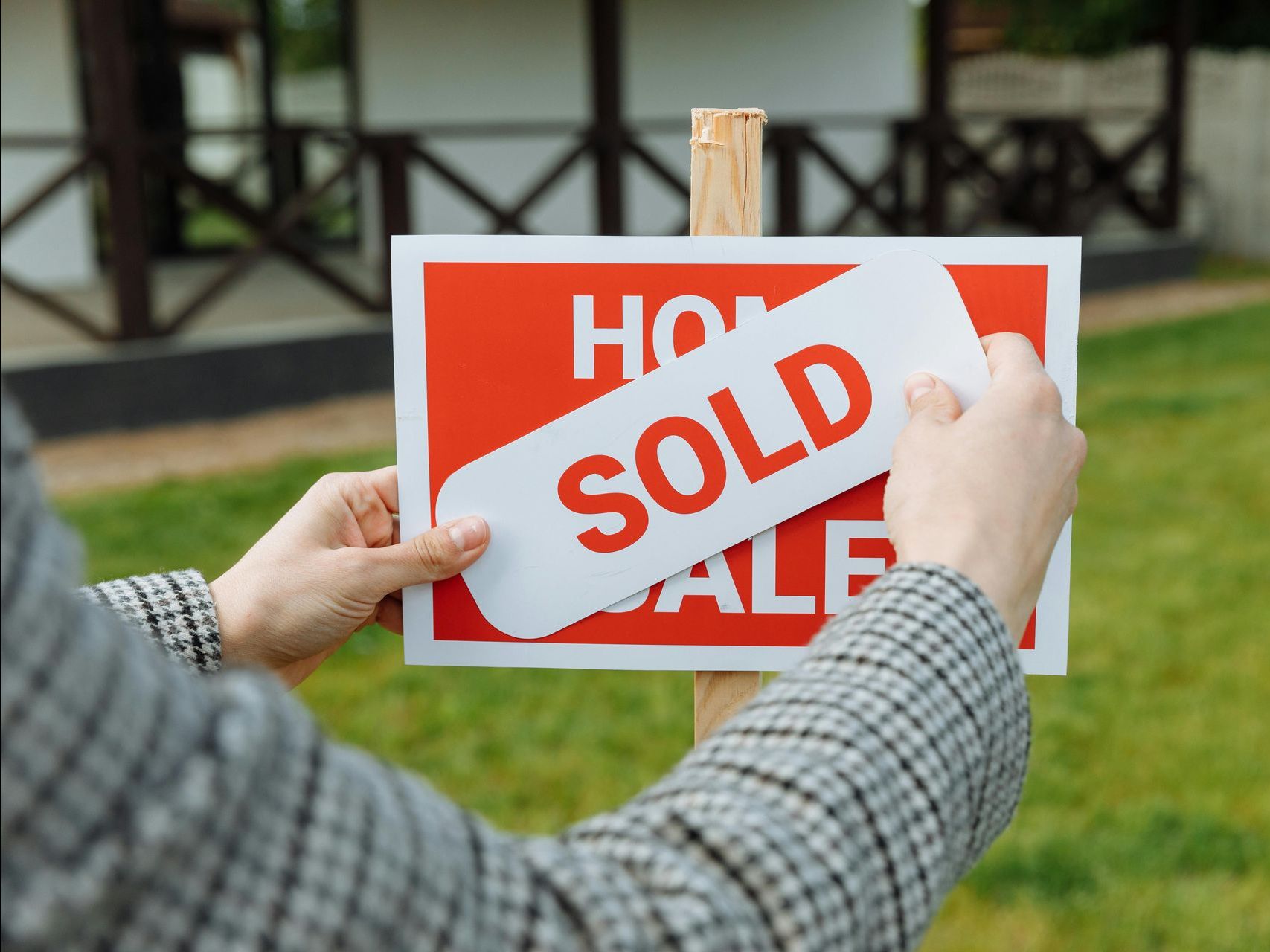 A person is holding a sold sign in front of a house