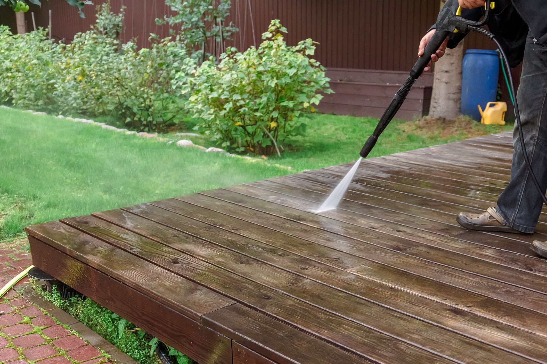 A man is cleaning a wooden deck with a high pressure washer.