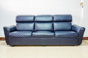 A black leather couch is sitting on a tiled floor in a living room.