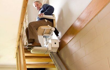 An elderly man is sitting on a stair lift.