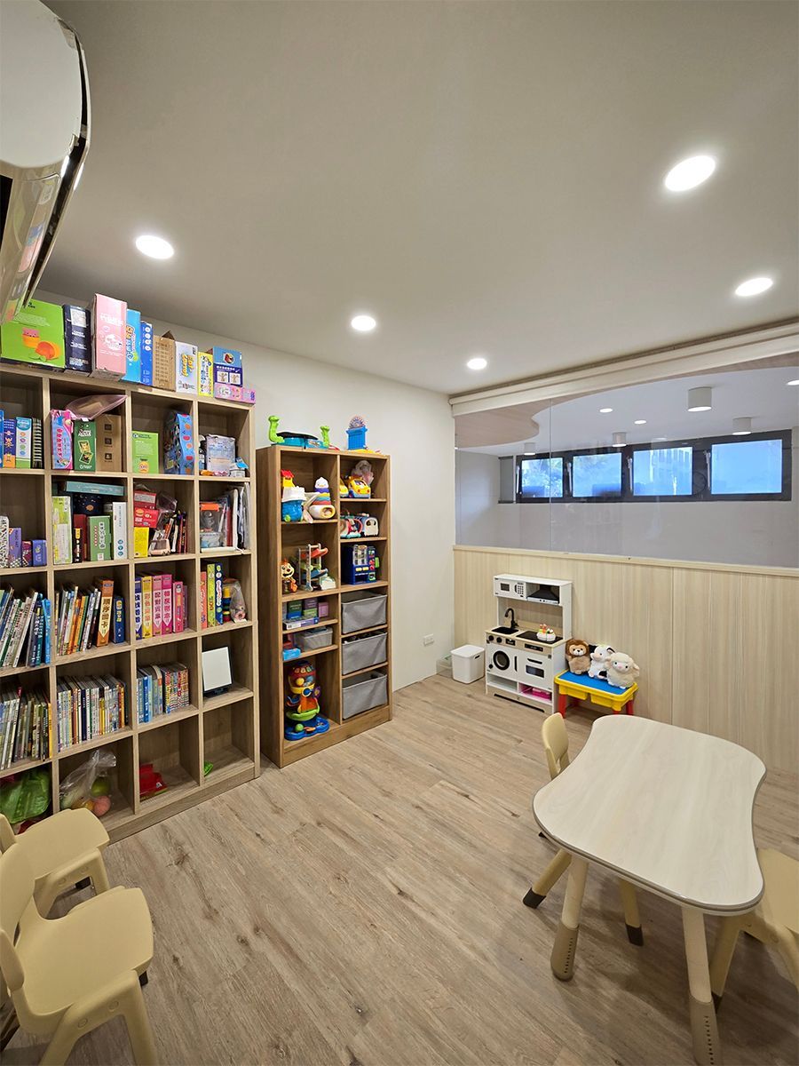 遊戲室有書架、小桌椅和玩具。木地板,白色牆壁。