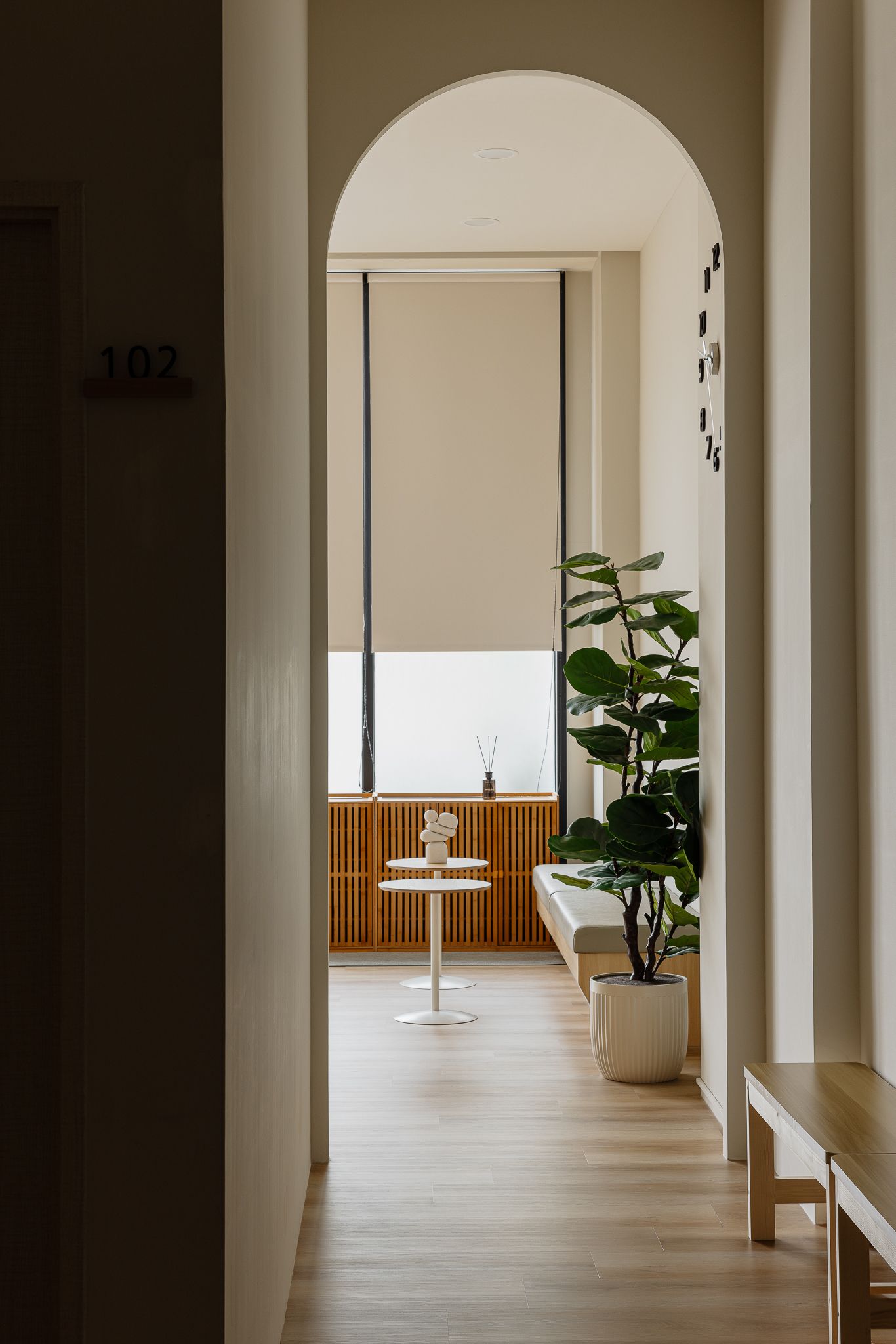 走廊呈拱形,通往一間光線充足的房間,房間內有窗戶、植物和木凳。