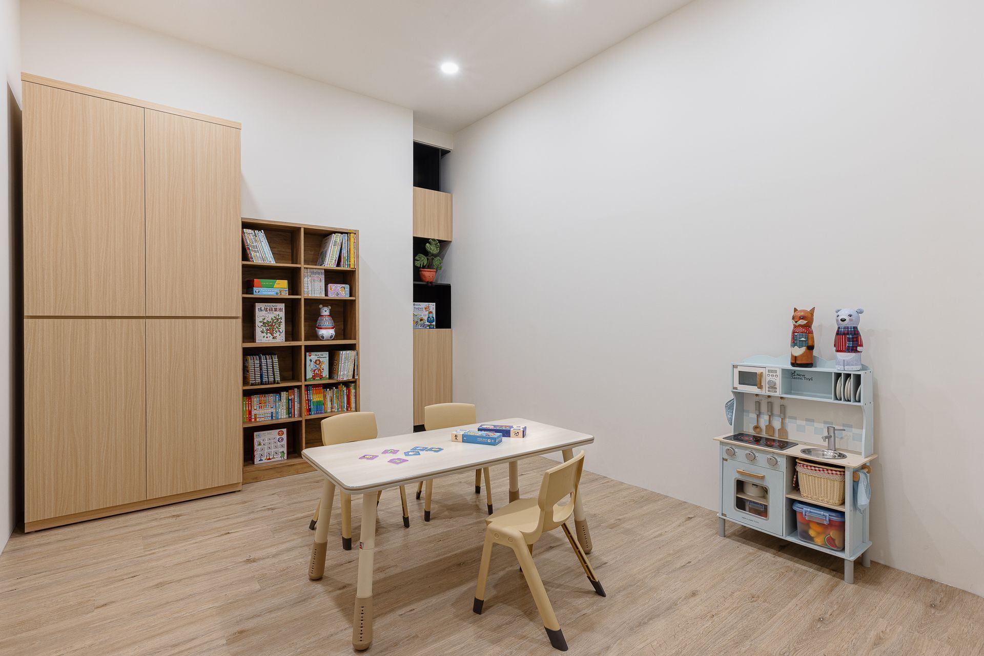 遊戲室配有淺色木質櫥櫃、桌子、椅子和靠白牆的玩具廚房。