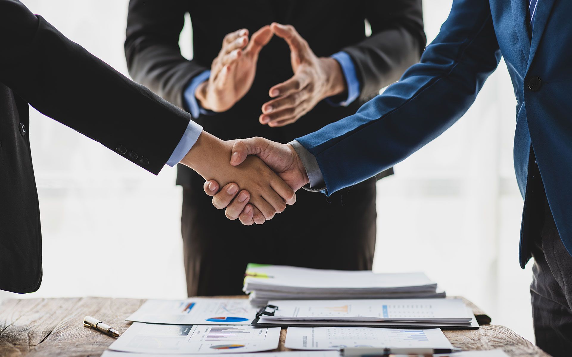 Three people meditating indoors, hands in mudra pose, eyes closed, on mats.
