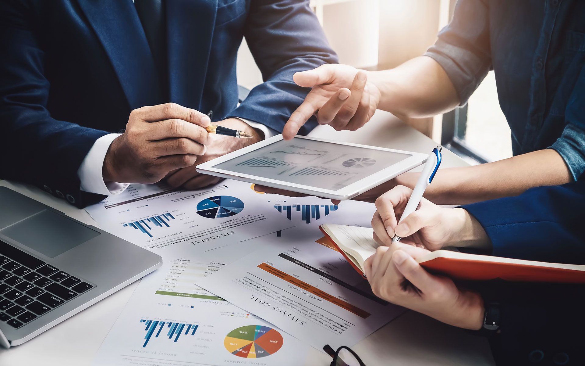 Business meeting: people reviewing charts and data on tablet and papers.