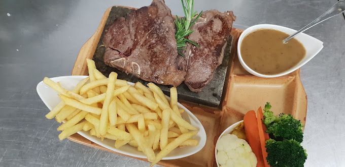 Une assiette de nourriture avec un steak, des frites et des légumes sur une table.