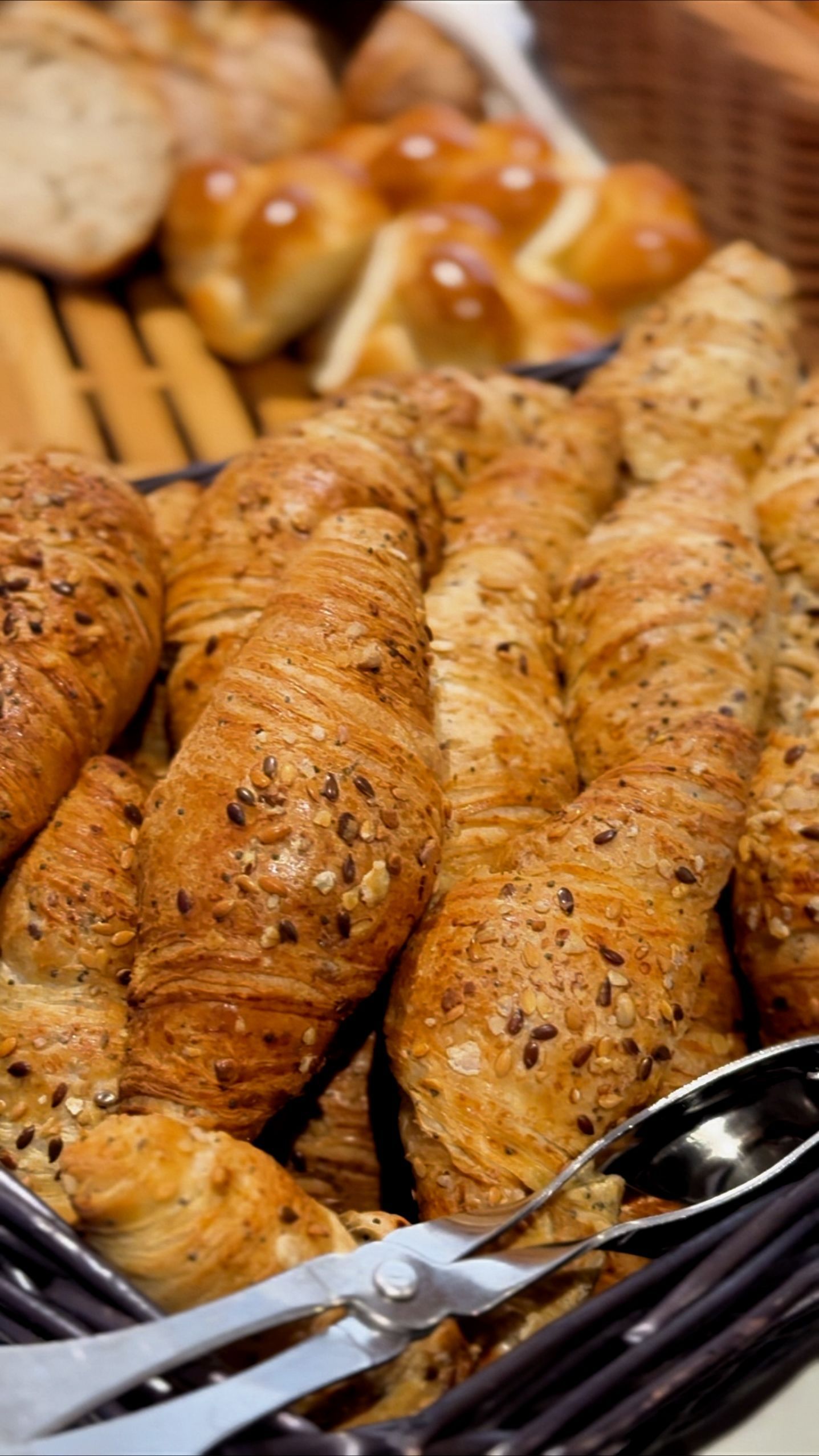 Un panier rempli de croissants et de petits pains avec des cuillères dedans.
