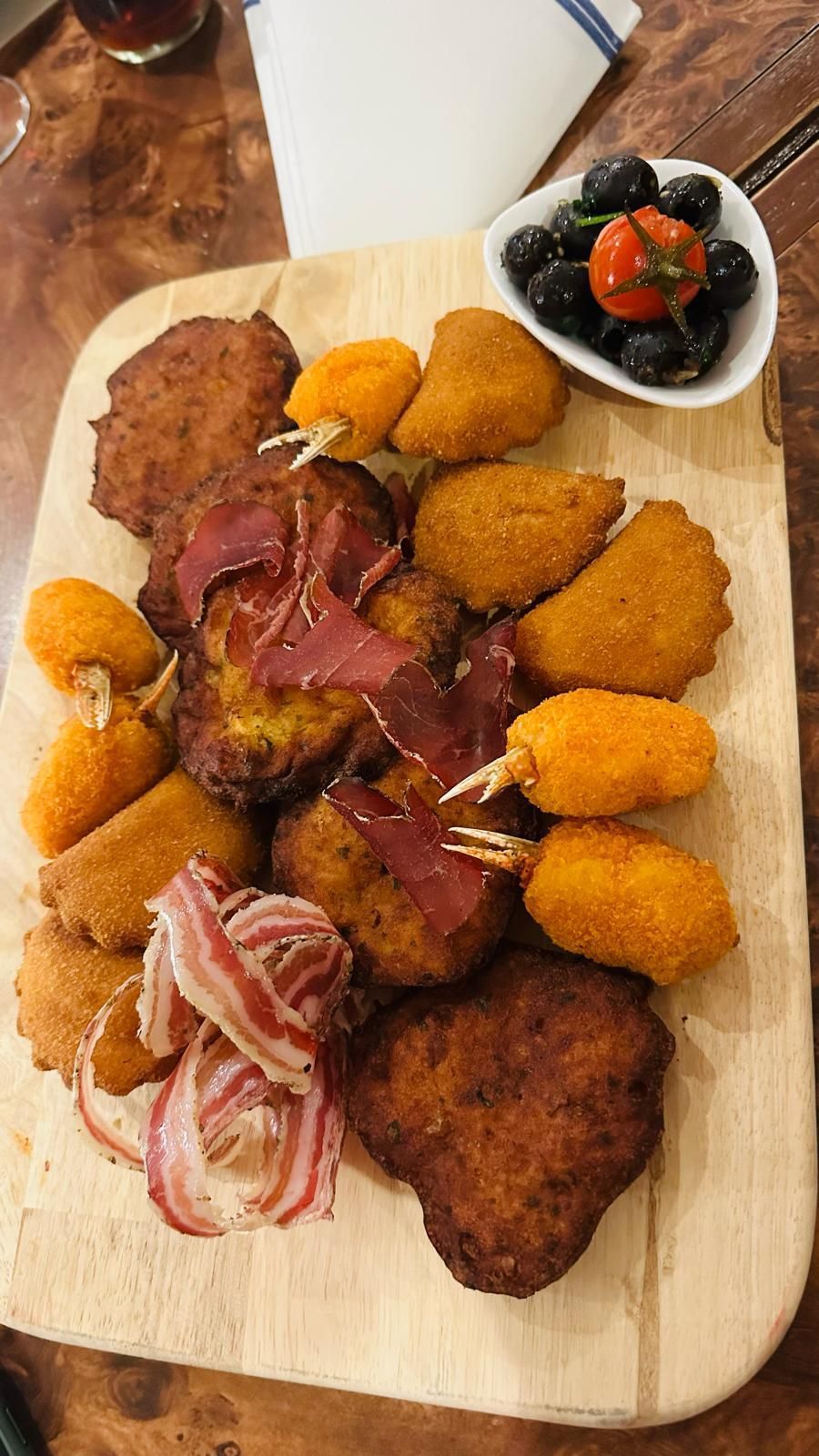 Une planche à découper en bois surmontée d'aliments frits et d'un bol d'olives.