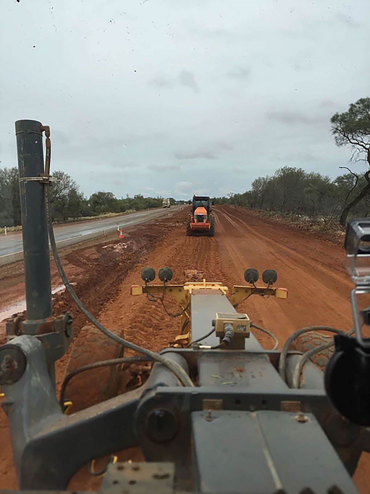 Two graders driving down a dirt road.