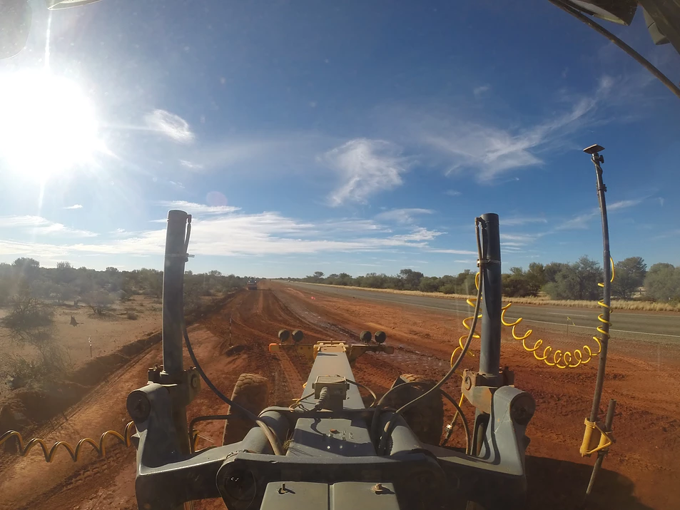 A grader driving down a dirt road.