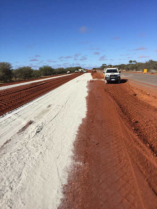 A white ute driving down a dirt road.