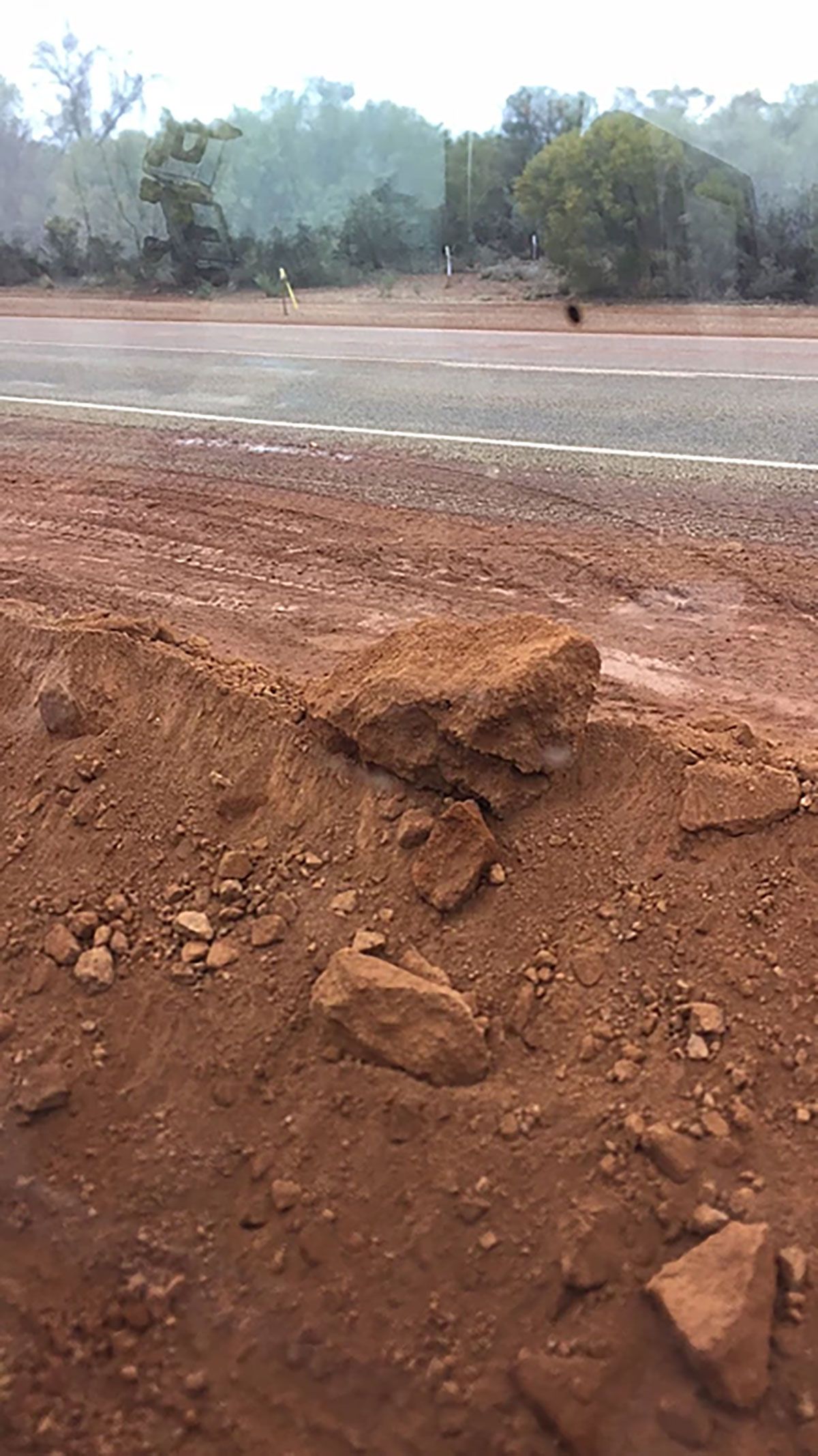 A large rock sitting on the side of a dirt road.