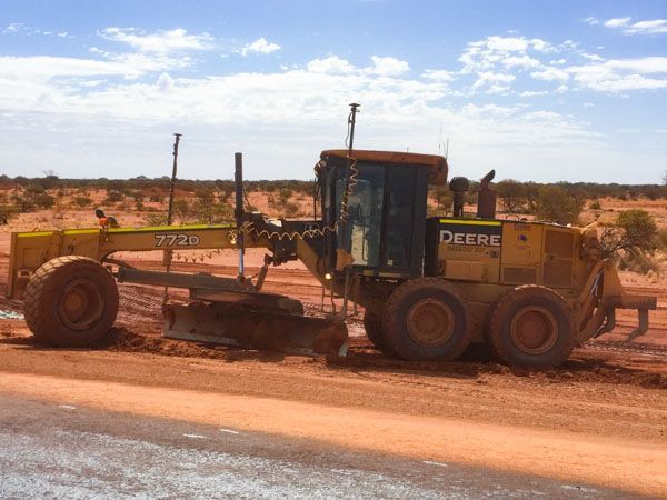 A John Deere grader working on a dirt road.