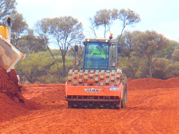 A roller driving down a dirt road.