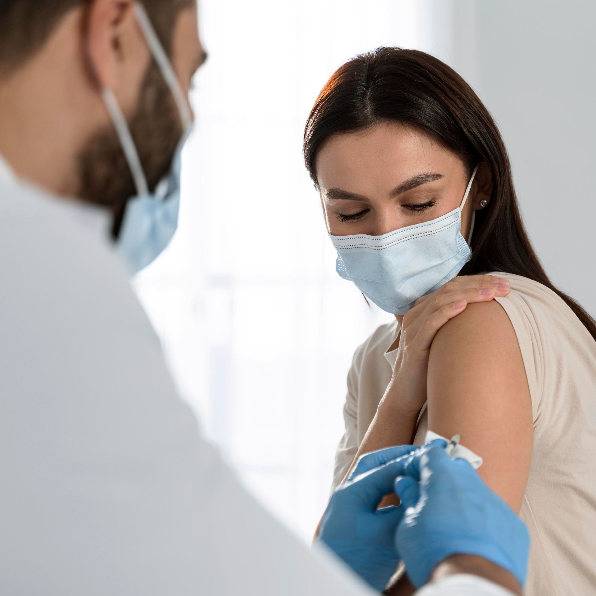 A woman wearing a mask is getting a vaccine from a doctor.