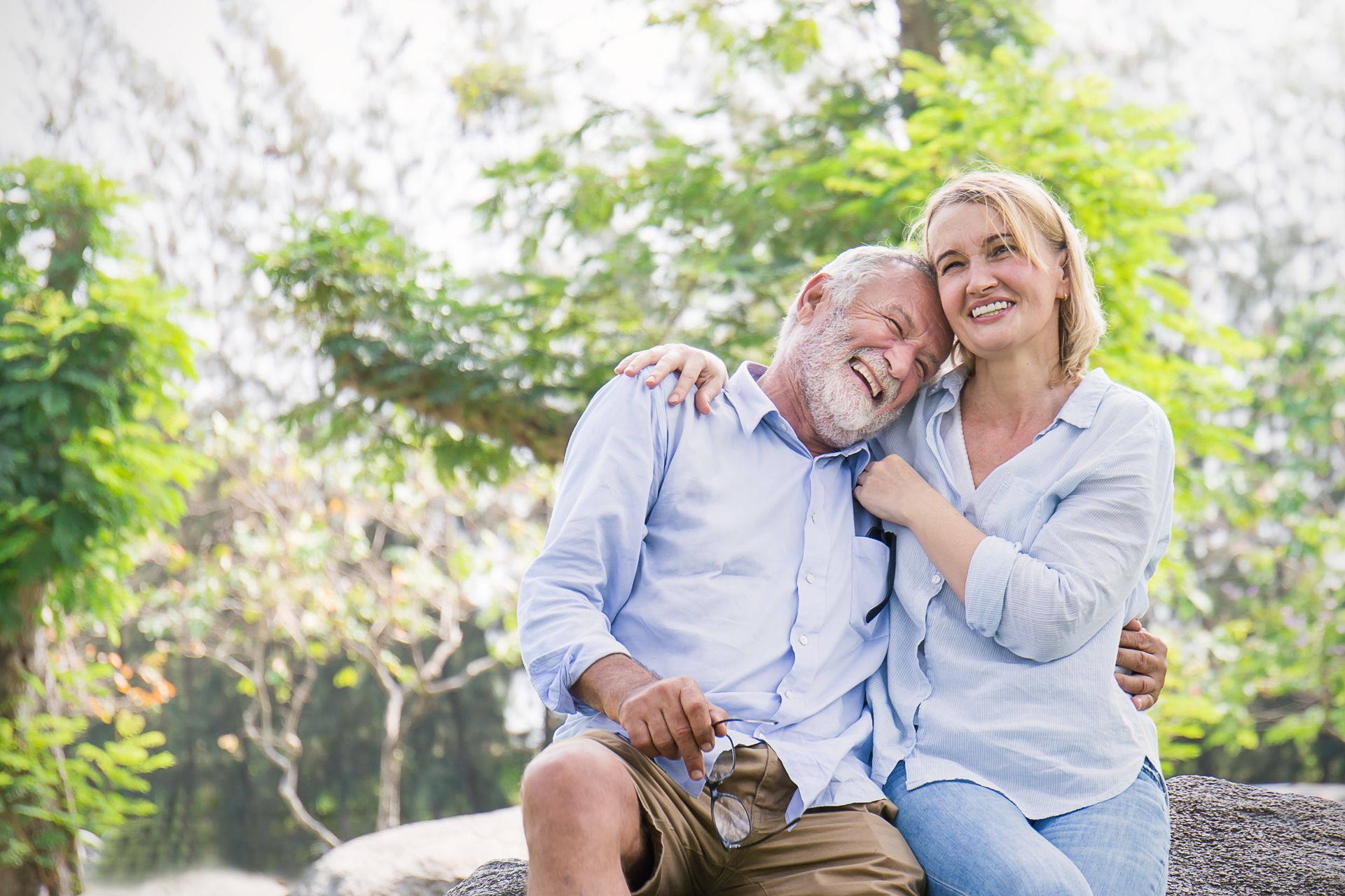 An elderly couple is sitting on a bench in a park.