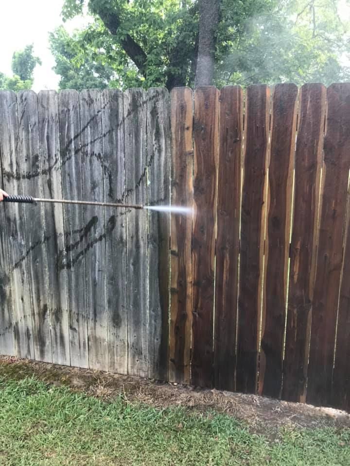 Power washing a wooden fence: half is stained brown, half is gray and dirty.
