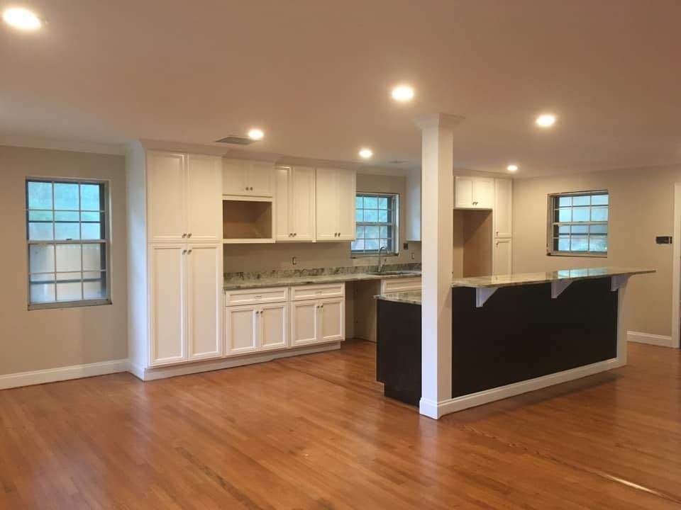 Spacious kitchen with white cabinets, granite countertops, dark island, and hardwood floors.