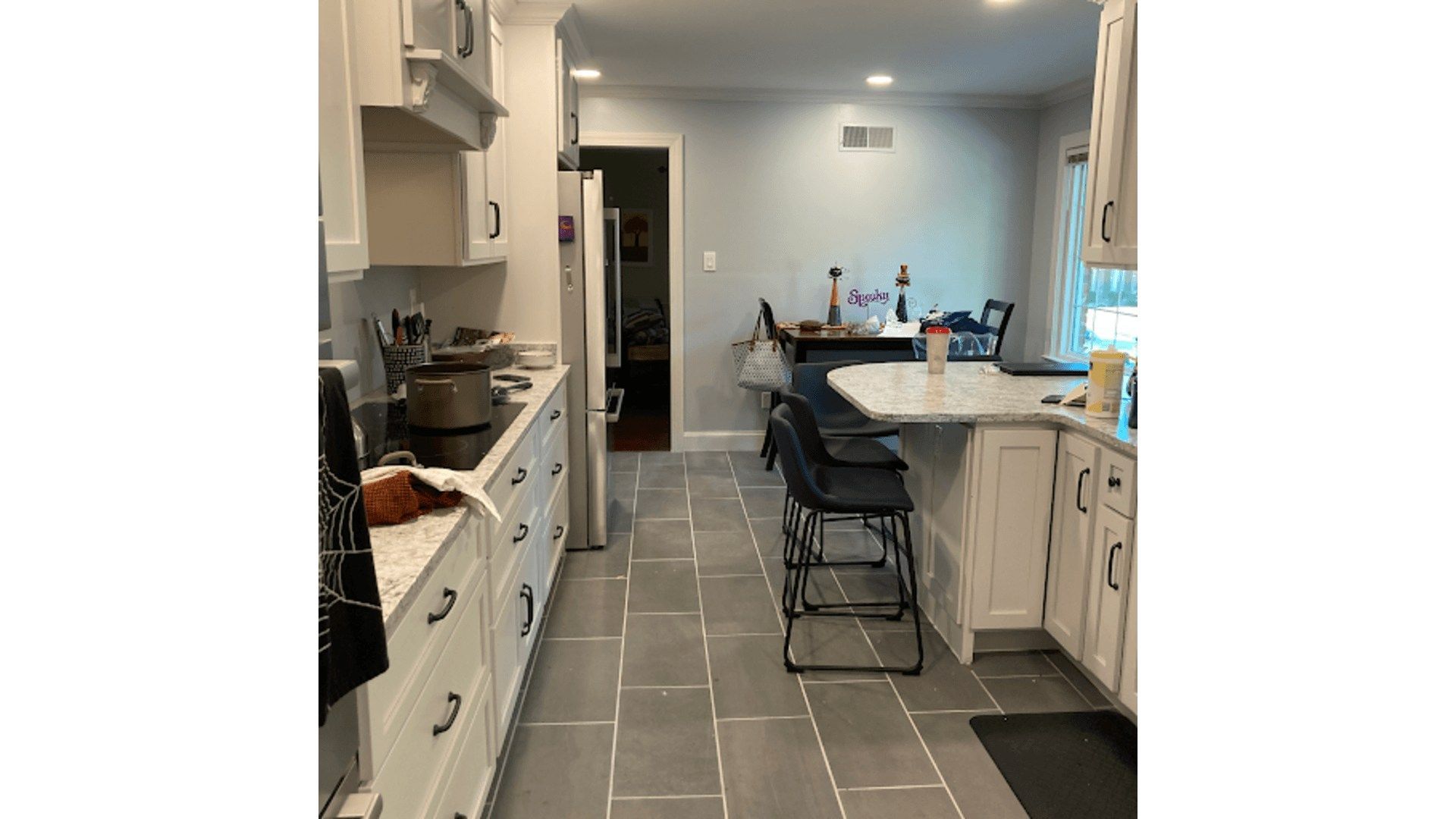 Gray-tiled kitchen with white cabinets, island, and appliances. The dining area is visible in the back.