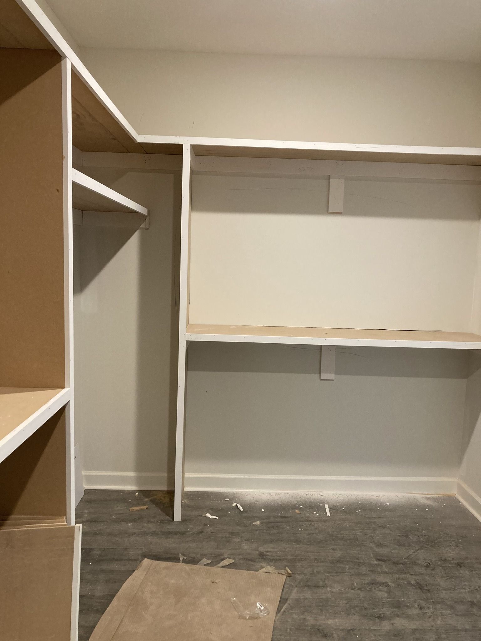 Empty closet with shelves and a rod, beige walls, and gray floor.