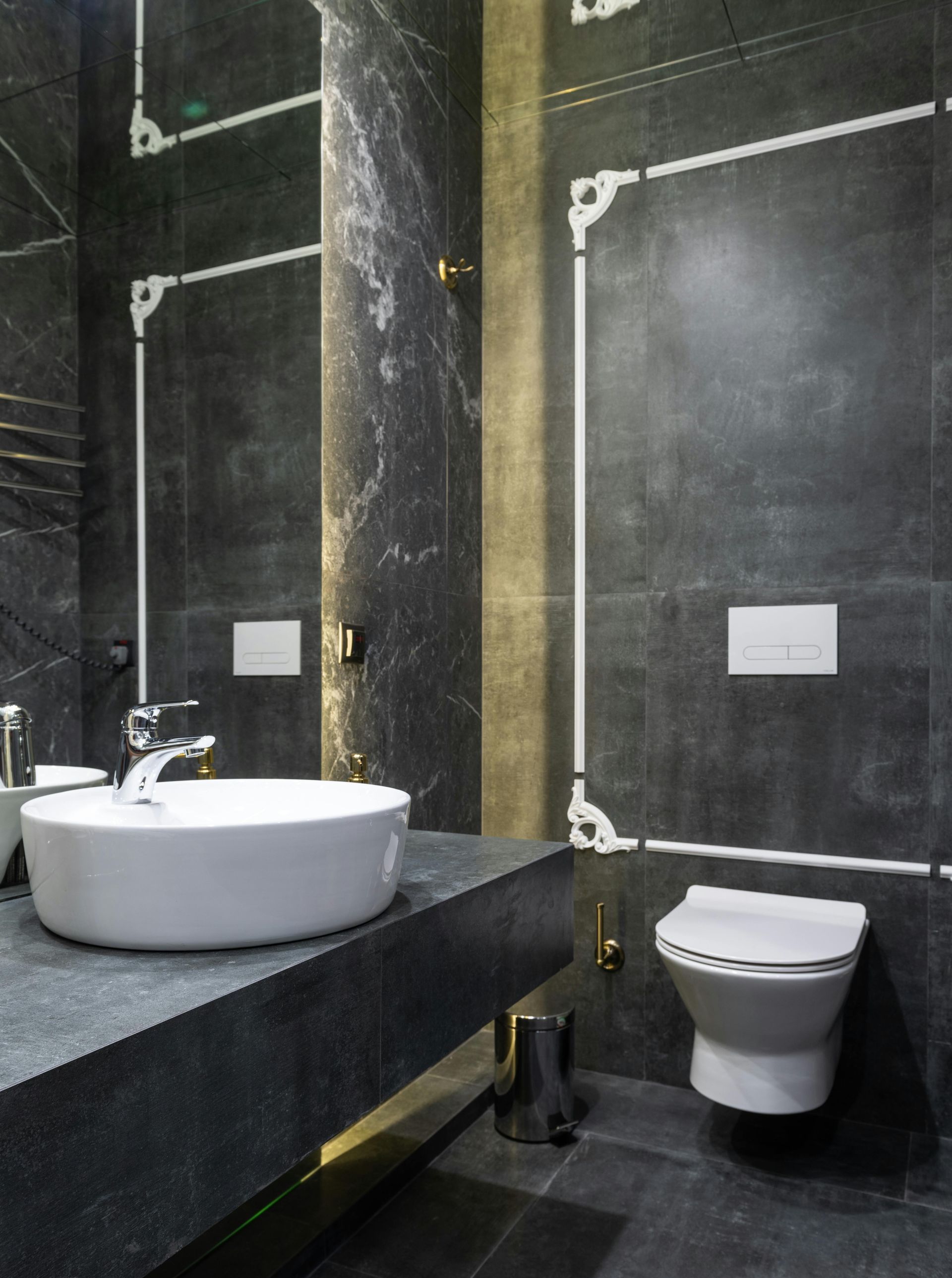 Modern bathroom with dark gray tile walls, white vessel sink, and toilet.