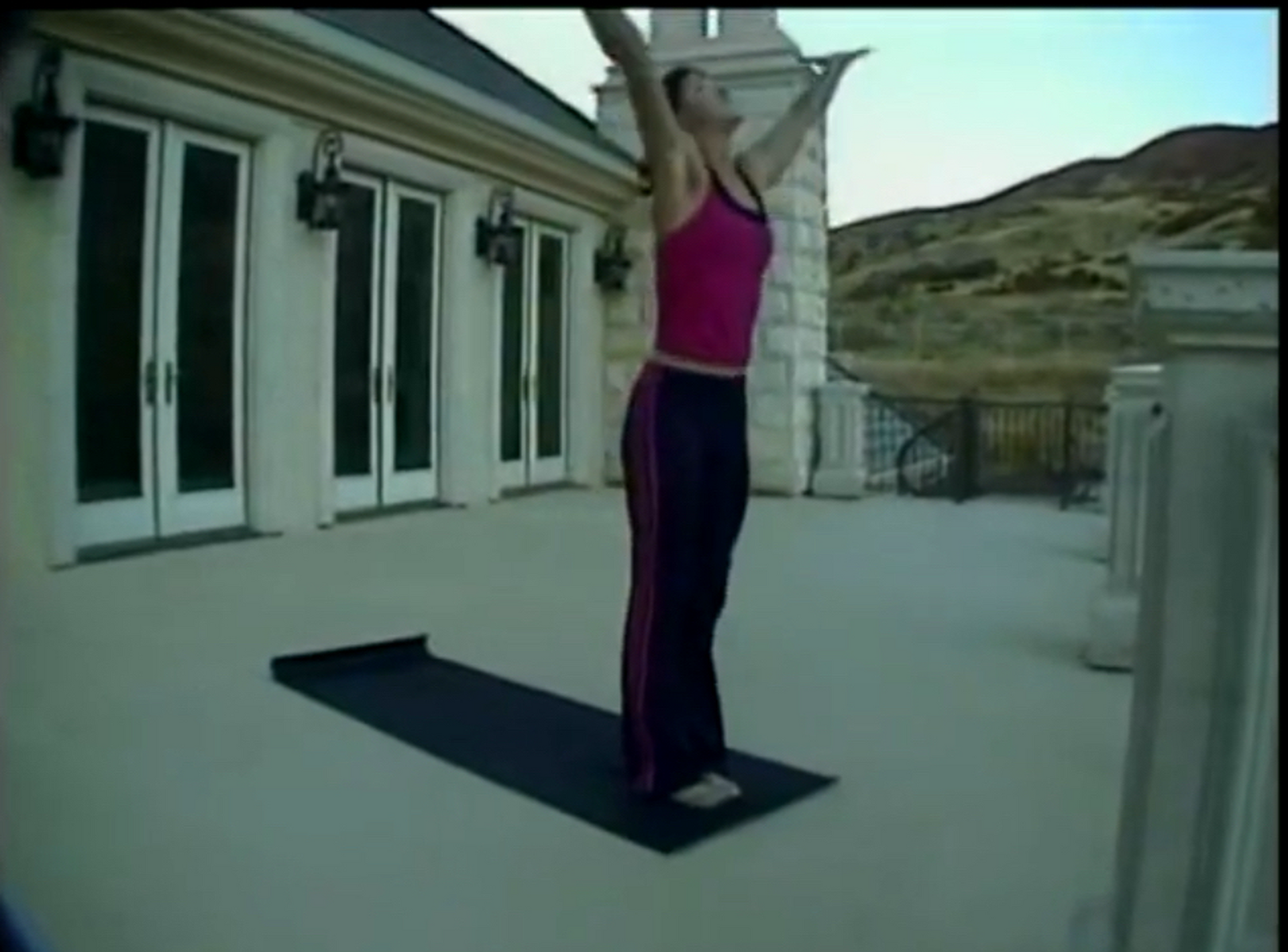 A woman is standing on a yoga mat with her arms outstretched
