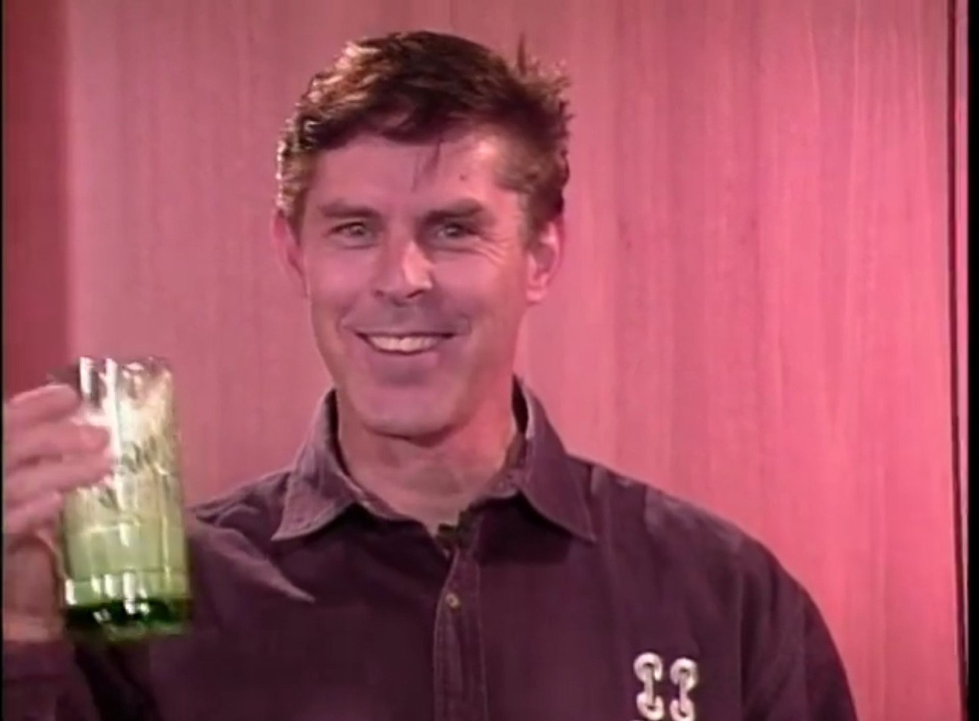 Tom Wright is holding a glass of green liquid in his hand.