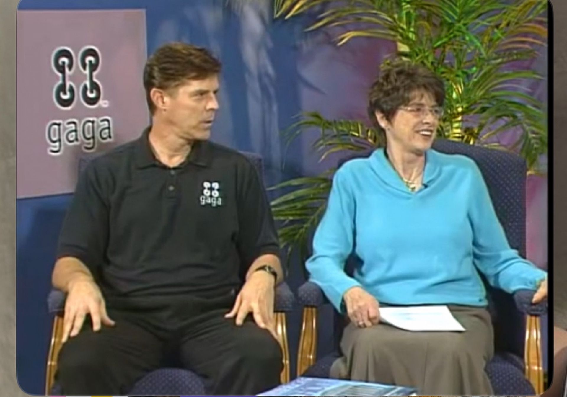 Tom Wright and a woman are sitting in front of a sign that says gaga