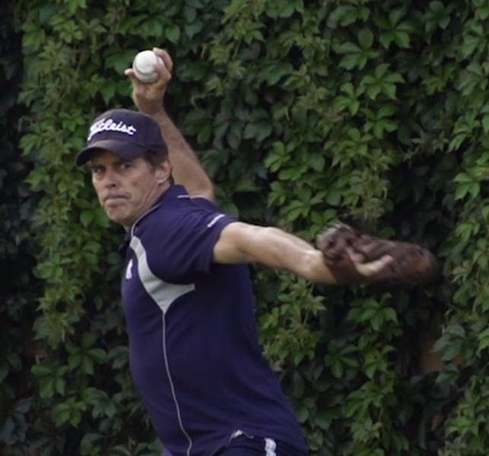 Tom Wright wearing a Titleist hat is throwing a baseball